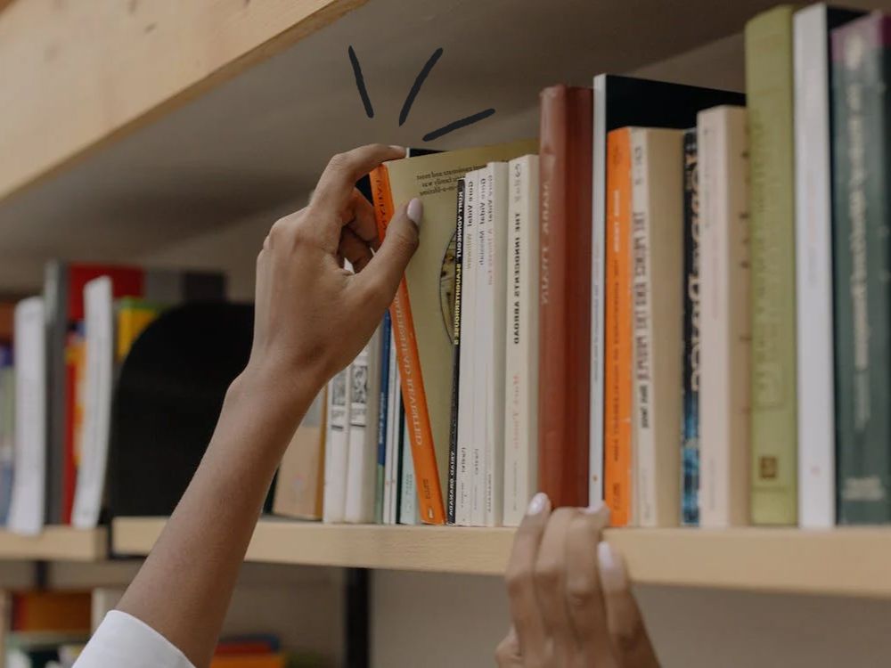 A hand grabbing a book from the shelf in a library